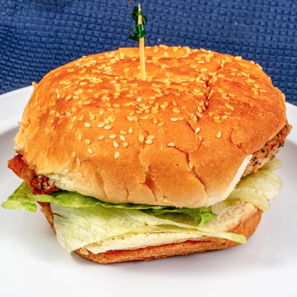 A Sunnyside Diner chicken sandwich with lettuce on a sesame seed bun, held by a toothpick.