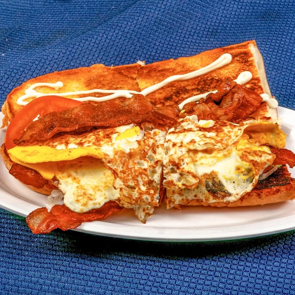 A Sunnyside Diner breakfast sandwich with bacon, fried eggs, cheese, and tomato on toasted bread.