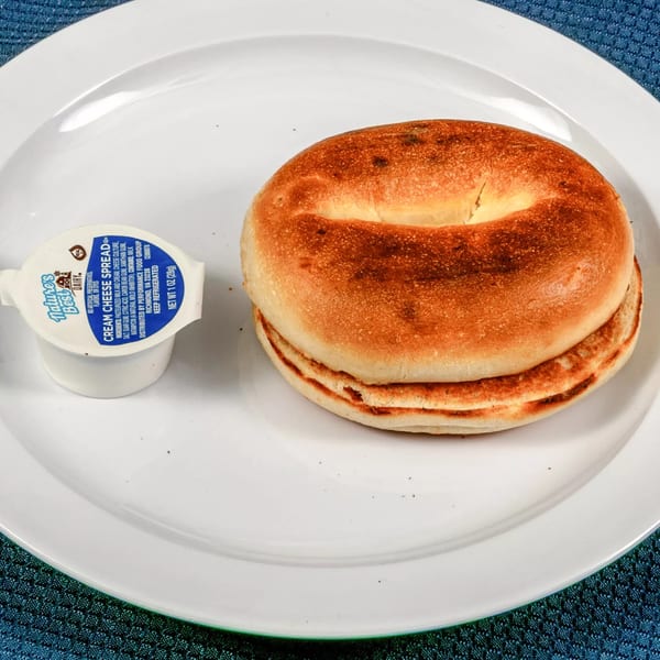 A toasted bagel and a small container of cream cheese on a white plate at Sunnyside Diner.