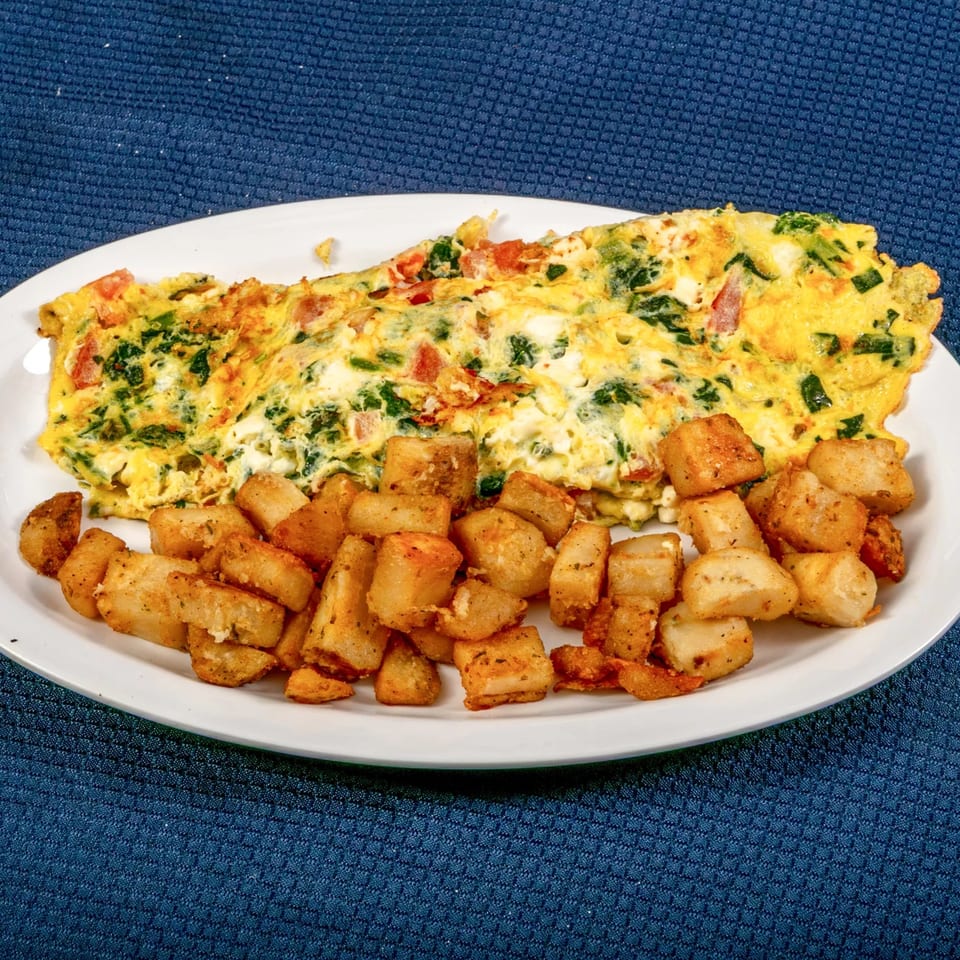 A Sunnyside Diner omelet with spinach, tomatoes, and cheese, served with crispy home fries.